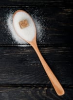 top view of a wooden spoon with white sugar and brown sugar cube on black background with copy space